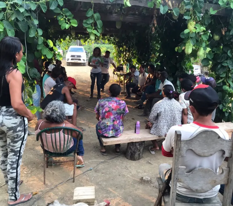 Tháscila falando para um grupo de moradores reunidos à sombra de um caramanchão