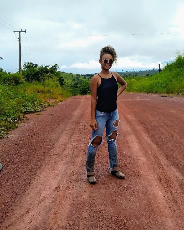 Tháscila numa estrada de terra vermelha, cercada de mato, na vicinal