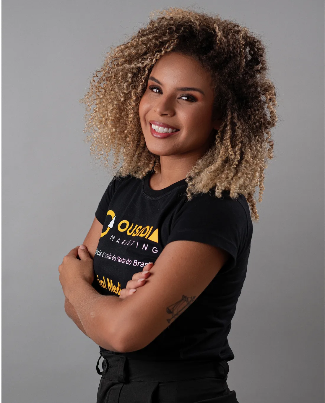 Tháscila Lawanda sorrindo, de braços cruzados, com a camiseta da Ousadia Marketing