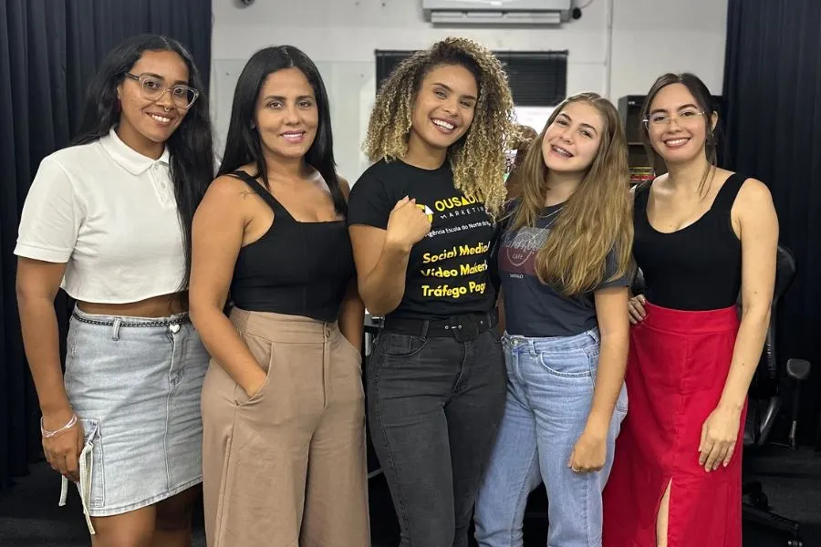 Cinco alunas sorrindo lado a lado na sala da Ousadia, uma delas com a camiseta da Ousadia Marketing