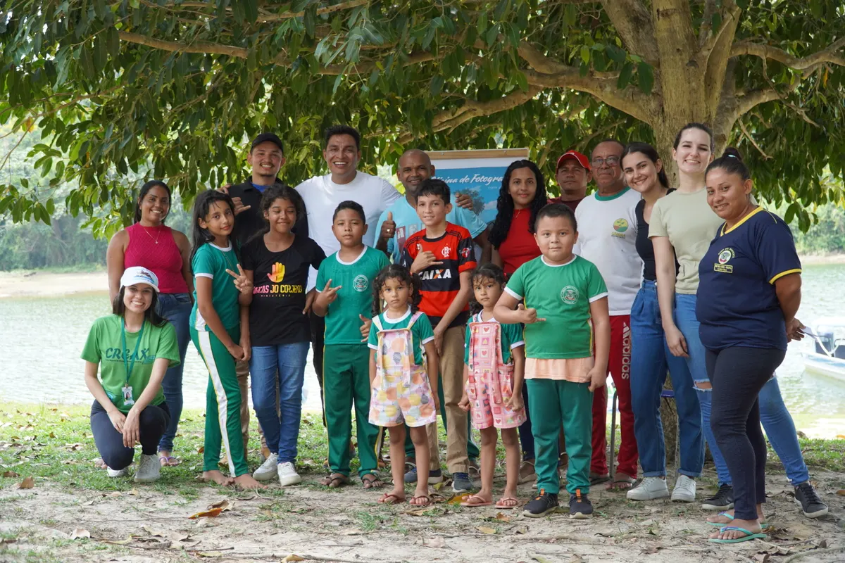 Jackson com alunos, crianças e educadores numa oficina de fotografia à sombra de uma árvore, na beira do rio
